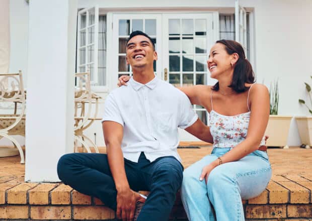 A couple holding each other with one arm while sitting on patio steps