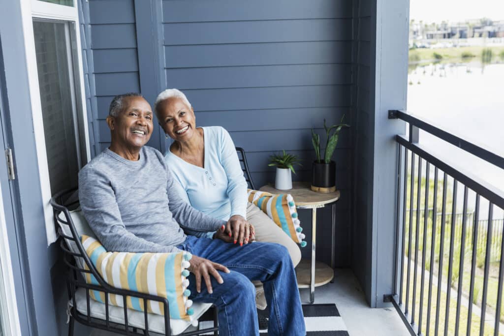 senior couple relaxing on porch, holding hand, smiling