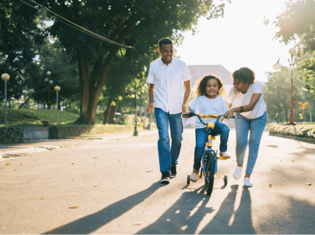 Parents teaching their child to ride a bike with training wheels